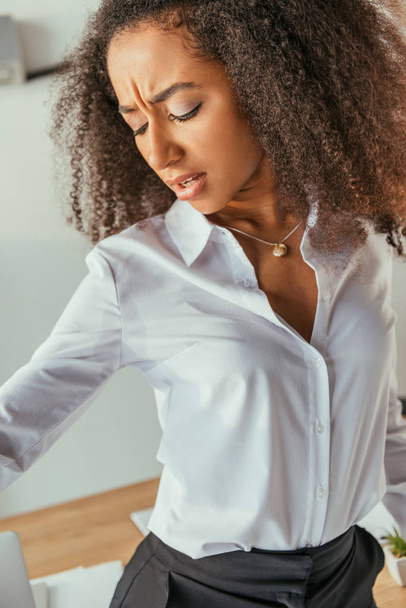 unzufriedene afrikanisch-amerikanische Geschäftsfrau schaut verschwitztes Hemd an, während sie unter Sommerhitze leidet - Foto, Bild