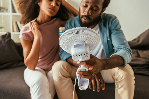 agotado afroamericano hombre y mujer sosteniendo soplado ventilador eléctrico mientras que sufre de calor de verano
 - Foto, Imagen