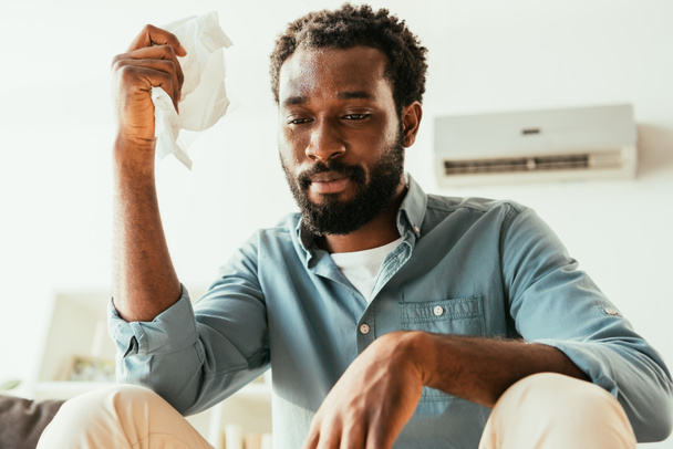 unhappy african american man holding napkin while suffering from summer heat at home - Foto, Imagem