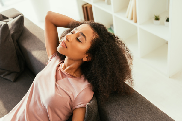 exhausted african american woman sitting on couch with closed eyes and suffering from heat - Photo, Image
