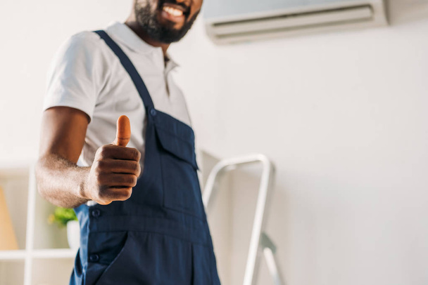 частичный вид улыбающегося африканского ремонтника, показывающего большой палец перед камерой
 - Фото, изображение