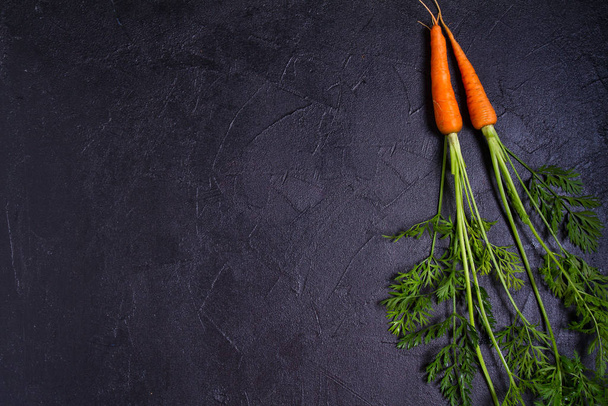 Carrots - root vegetables on a black background. Summer farm vegetables. Food background, layout, room for text - Fotografie, Obrázek