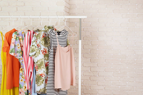 Women's hip clothing store interior concept. Row of different colorful female clothes hanging on rack in hipster fashion show room in shopping mall. White brick wall background. Copy space. - Photo, Image