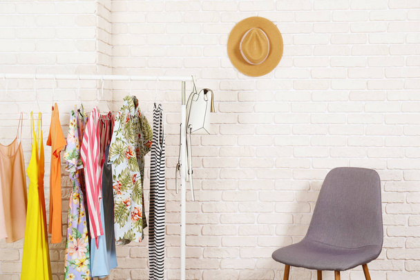 Women's hip clothing store interior concept. Row of different colorful female clothes hanging on rack in hipster fashion show room in shopping mall. White brick wall background. Copy space. - Foto, afbeelding