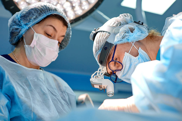 Kirurgi ja hänen avustajansa tekevät kauneusleikkauksia sairaalan leikkaussalissa. Kirurgi naamiossa yllään loupes aikana lääketieteellisen hankinnan
. - Valokuva, kuva