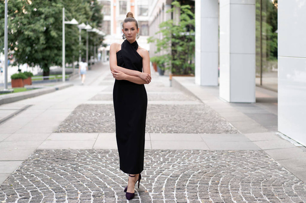 beautiful slender european girl 30 years old in a black dress posing on the street near boutiques. Beautiful weather and mood. Stylish beautiful model in full growth. - Foto, Imagem