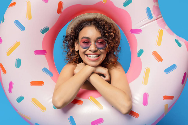 fröhliches schwarzes Mädchen lächelt durch Donut aufblasbaren Ring - Foto, Bild