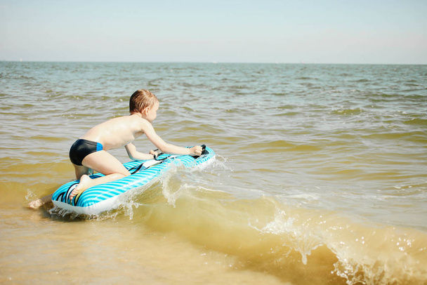 Garçon avec matelas gonflable bleu vif nage dans la mer
 - Photo, image