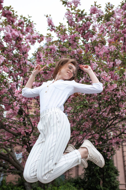 hermosa joven feliz mujer en una blusa y vasos cerca de las flores de cerezo
 - Foto, Imagen