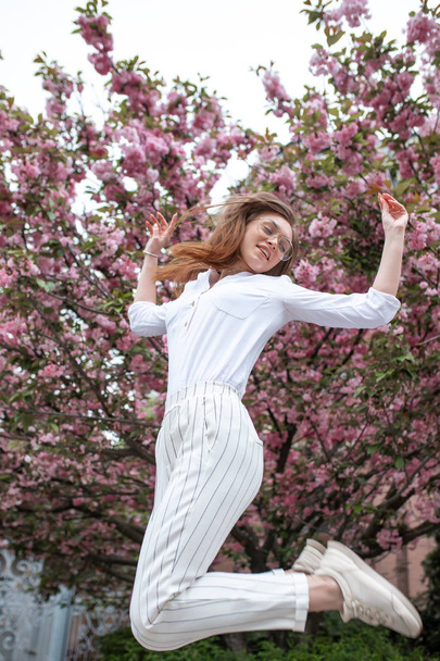 hermosa joven feliz mujer en una blusa y vasos cerca de las flores de cerezo
 - Foto, Imagen