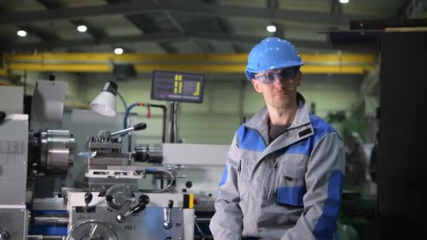 Ικανοποιημένος Καυκάσιος μηχανικός επεξεργασίας μετάλλων στο μπροστινό μέρος της μηχανής τόρνος μετάλλων στη γραμμή παραγωγής - Πλάνα, βίντεο