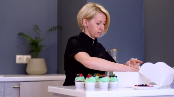 Kezében női péksütemény szakács csomagolás frissen készült Cupcakes vajkrém fagyosan a díszdobozban és árukapcsolás azt szalag, nagy látószögű nézet - Felvétel, videó
