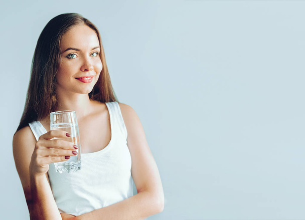 Mode de vie sain. Une jeune femme montre un verre d'eau. Une fille boit de l'eau. Portrait de modèle féminin souriant heureux tenant verre transparent d'eau. Santé, Beauté, Diète concept
 - Photo, image