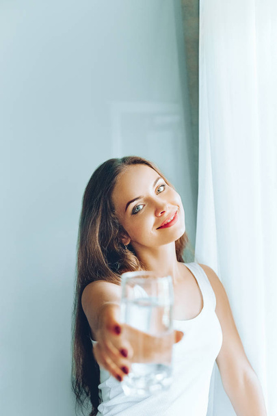 Closeup young woman show glass of water. Portrait of happy smiling female model  holding transparent glass of water.Healthy lifestyle. Beauty, Diet concept - Photo, image