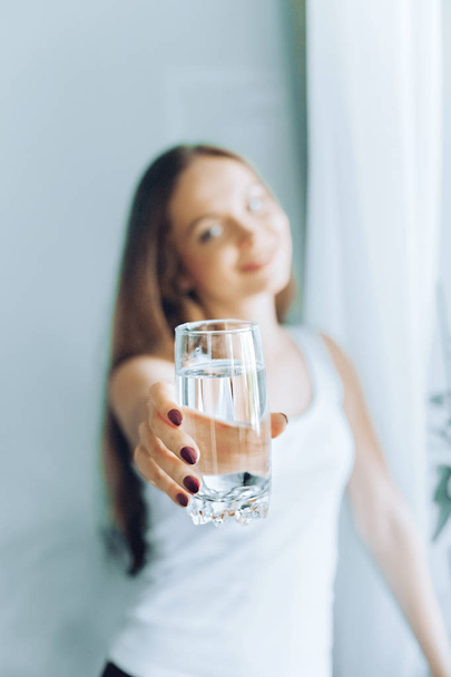 Closeup young woman show glass of water. Portrait of happy smiling female model  holding transparent glass of water.Healthy lifestyle. Beauty, Diet concept - Photo, image