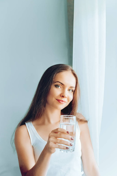 Healthy lifestyle.Young woman drinking from a glass of  fresh water. Healthcare. Drinks. Portrait of happy smiling female model holding transparent glass. Health,Beauty,Diet concept. Healthy eating. - Zdjęcie, obraz