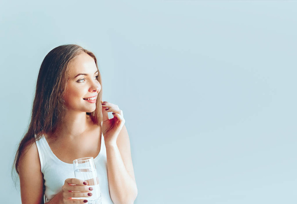 タラの肝油オメガ3でビタミンピルを服用し、朝に淡水のグラスを保持する美しい笑顔の女性.栄養補助食品。健康的な食事, ライフスタイル. - 写真・画像