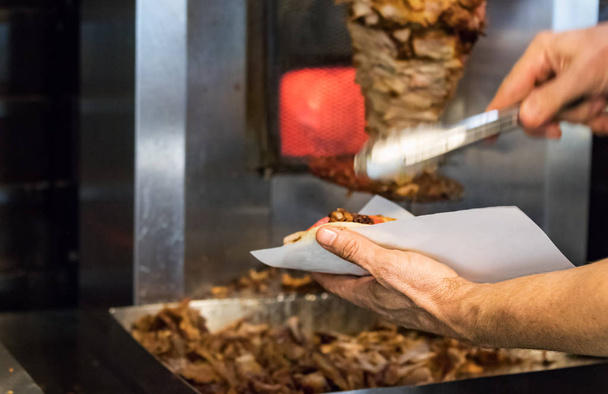 A man hand making a pita sandwich with pork gyros in a Greek restaurant. - Fotoğraf, Görsel
