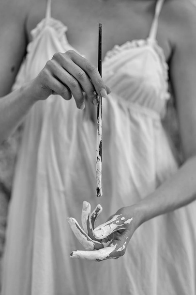 Cuadro en blanco y negro de un torso de una joven sosteniendo un pincel y pintando su mano con pintura blanca
. - Foto, Imagen