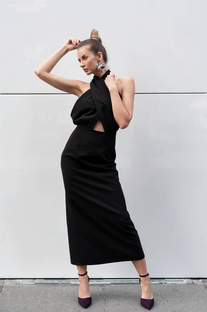 beautiful slender european girl 30 years of age in a black dress posing on the street near the white wall. Beautiful weather and mood. Stylish beautiful model. - Valokuva, kuva