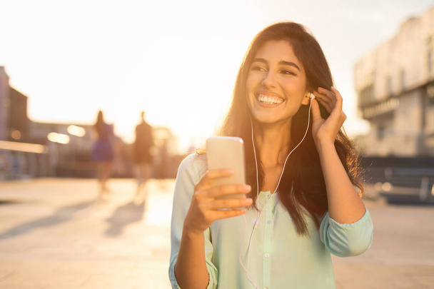 Mujer feliz caminando por la ciudad y escuchando música por teléfono
 - Foto, imagen