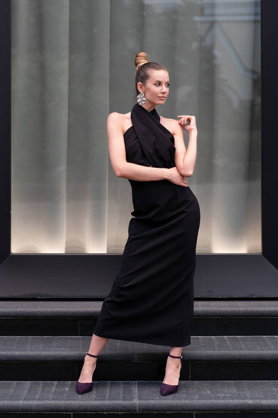 Beautiful girl in a long black dress posing in full growth near the boutique. Graceful interesting poses. - Фото, зображення