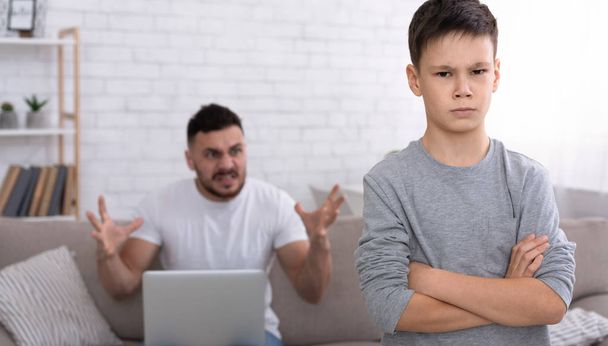 Trauriger kleiner Junge blickt in die Kamera, wütender Vater mit Laptop brüllt ihn an - Foto, Bild