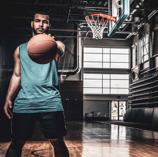 Black basketball player holds a ball over a hoop in a basketball - Φωτογραφία, εικόνα