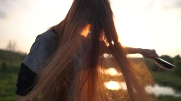 La chica cepilla el pelo largo y rojo en la naturaleza de cerca al atardecer en cámara lenta
 - Imágenes, Vídeo