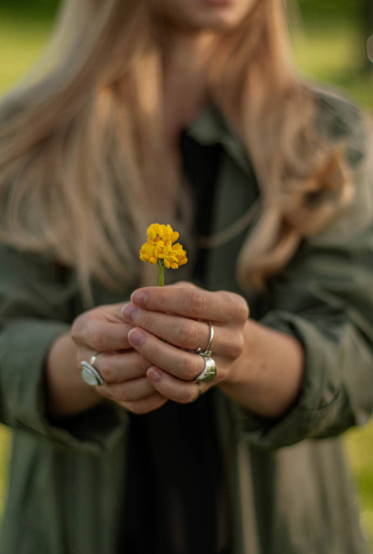Beautiful woman with long hair holding flower. Hands with rings stylish boho accessories. No focus  - Foto, Bild
