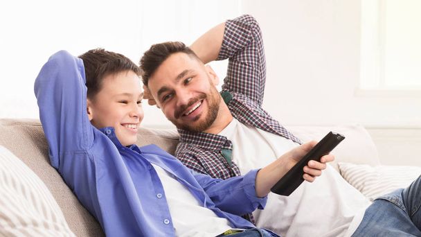 Menino alegre trocando controle remoto, sentado em casa com o pai
 - Foto, Imagem