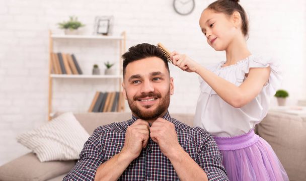 Cute little girl combing her handsome father and smiling - Photo, Image
