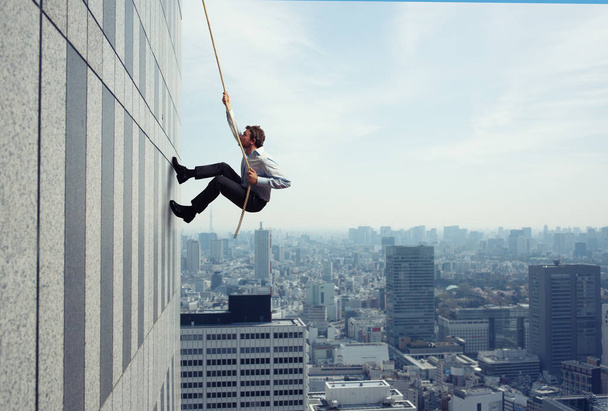 Ο επιχειρηματίας σκαρφαλώνει σε ένα κτίριο με σχοινί. Έννοια προσδιορισμού - Φωτογραφία, εικόνα