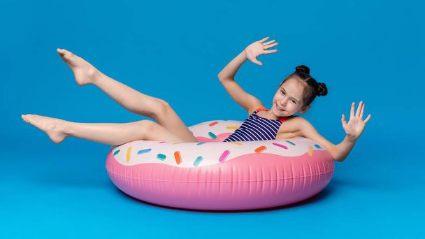 glückliches kleines Mädchen schwimmt auf Donut förmigen rosa aufblasbaren Ring - Foto, Bild