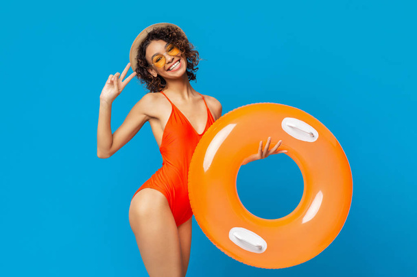 fröhliches schwarzes Mädchen in Badebekleidung mit Schwimmring und Friedensgeste - Foto, Bild