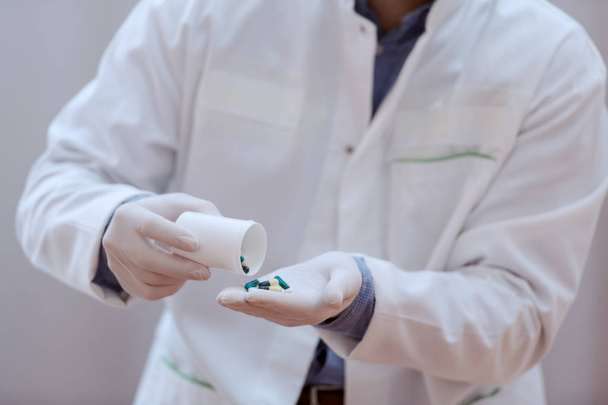 Close up of male doctor in white uniform and with rubber gloves on holding capsules in hands. - Valokuva, kuva