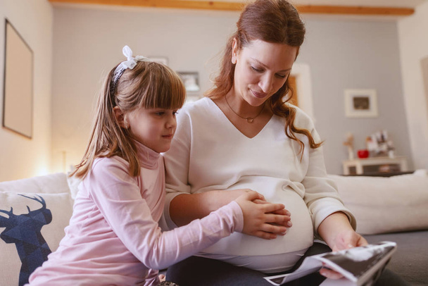 Bella mamma incinta guardando con la figlia immagini ad ultrasuoni del suo bambino non ancora nato. Ragazza che tiene la mano sulla pancia
. - Foto, immagini