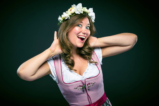 Beautiful young woman in traditional bavarian dirndl and floral wreath smiling at camera isolated on grey - Zdjęcie, obraz