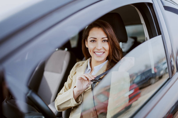 Gorgeous Caucasian brunette dressed smart casual sitting in her car and fastening seat belt. - Φωτογραφία, εικόνα