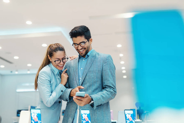 Cute multicultural couple dressed elegant choosing new smart phone in tech store. Man pointing at smart phone. - Photo, Image