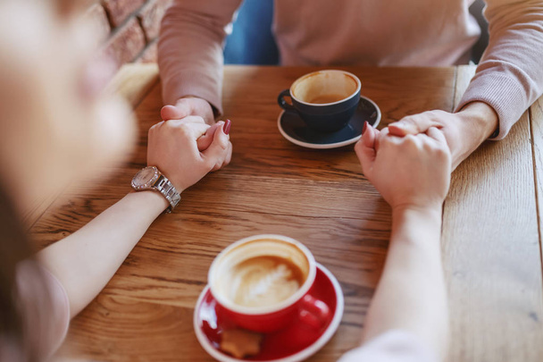 Jovem casal apaixonado sentado na cafetaria e de mãos dadas, copos com café na mesa
 - Foto, Imagem