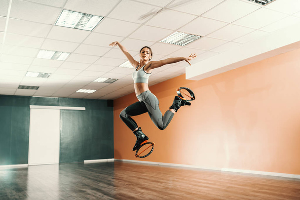 Mooie fit Kaukasische brunette in sportkleding springen op kangoo jumps schoeisel in sportschool. - Foto, afbeelding