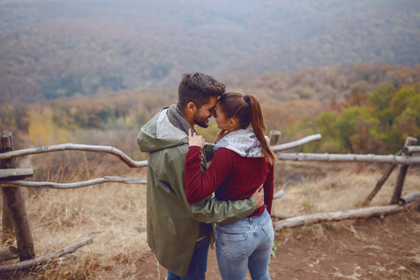 Cute multicultural couple in love dressed casual hugging while standing in nature. Backs turned. Autumn season. - Photo, Image