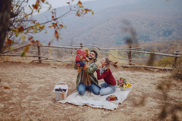 attraktives multikulturelles Paar, das auf einer Decke sitzt und mit seinem Hund spielt. Picknick beim Herbstkonzept. - Foto, Bild