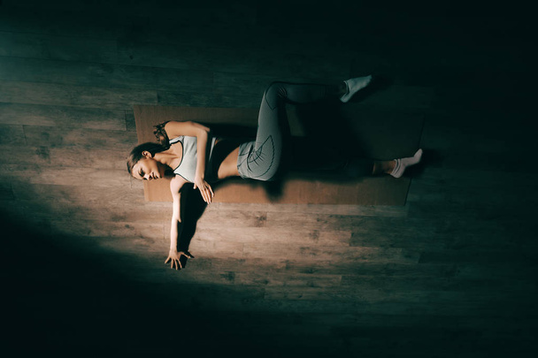 Top view of young Caucasian brunette lying down on mat and stretching in gym at night. - Photo, Image