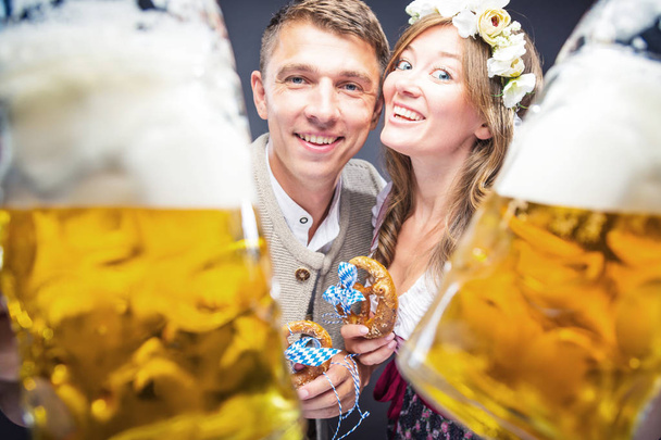 happy young couple holding pretzels and glasses of beer - Fotografie, Obrázek