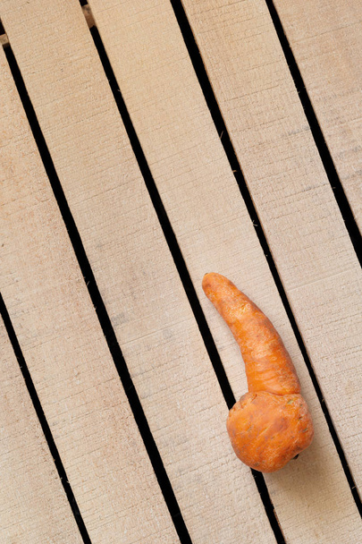 Уродливая морковка на фоне деревянной коробки. Органические продукты питания, необычные деформированные фрукты и овощи, деформированные продукты, нулевая концепция отходов. Вид сверху, копировальное пространство, вертикальное
. - Фото, изображение