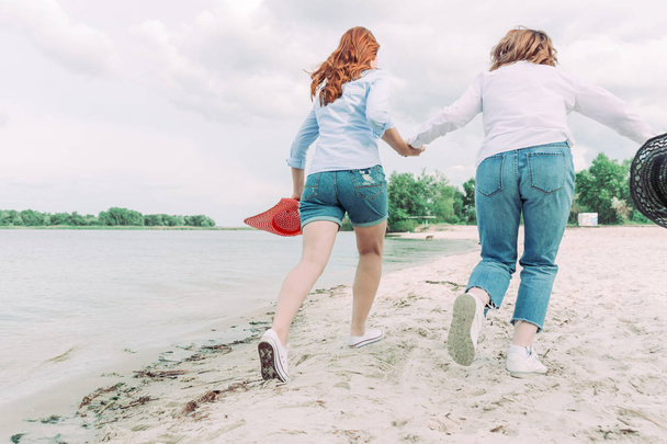 Két fiatal nő barátai futnak a tengerparton. Hátulnézet. - Fotó, kép