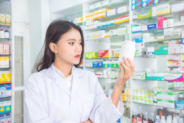 Piękny farmaceuta gospodarstwa i patrząc na butelkę leku - Zdjęcie, obraz