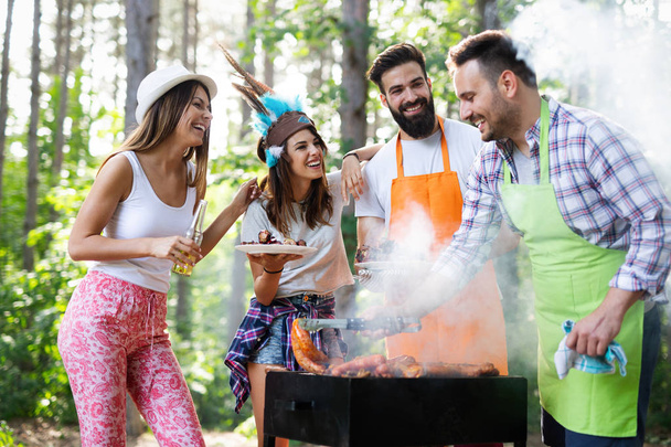 Happy friends making barbecue and having lunch in the nature - Фото, изображение